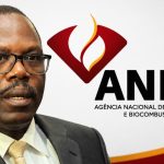Retrato de Paulino Jerónimo, Presidente do Conselho de Administração da ANPG, em plano médio, olhando ligeiramente para o lado. Ele usa óculos de armação preta, fato cinzento, camisa clara e gravata amarela estampada. À direita, ao fundo, destaca-se o logótipo oficial da ANPG (Agência Nacional de Petróleo, Gás e Biocombustíveis) com o seu símbolo vermelho e dourado sobre um fundo branco.